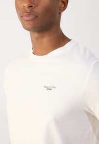 Witte katoenen t-shirt met een ronde hals en korte mouwen, met een kleine zwarte printtekst "Marc O'Polo DENIM" op de linkerkant van de borst.