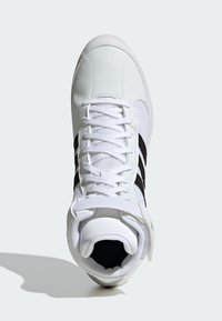 White athletic shoe with a textured leather upper, three black stripes on the side, and a mesh tongue. Features laces and an ankle strap.