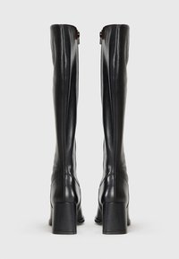 Bottes noires arrivant au genou en cuir lisse, dotées d'un talon carré et d'un détail de fermeture éclair en haut. Design épuré avec un minimum de coutures.
