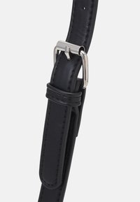 Czarny pasek ze skóry o gładkiej fakturze, z srebrną metalową klamrą i detalem przeszycia. Regulowana długość z wieloma otworami.