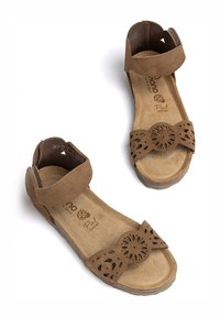 Braune Wildledersandalen mit einem Knöchelriemen, lasergefrästem Blumenmuster auf der Vorderseite, gepolsterter Innensohle und einer niedrigen, strukturierten Sohle.