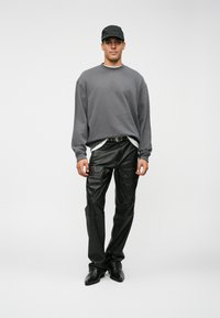 Γκρι φούτερ με λαιμόκοψη, μαύρο δερμάτινο παντελόνι, μαύρο καπέλο και παπούτσια. Το παντελόνι έχει γυαλιστερή υφή, το φούτερ είναι φαρδύ, με στρώσεις.