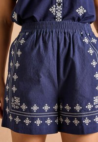 Marineblå linnedshorts med hvidt broderet snefnugmønster langs bunden og lommer, med elastisk talje for pasform.