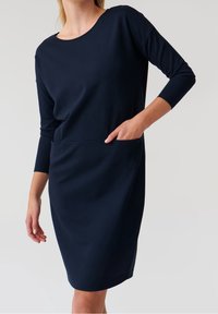 Marinblå klänning i mjukt tyg, med rund halsringning, trekvartsärmar och sidofickor för extra funktionalitet.