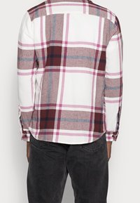 Camicia di flanella a scacchi bianca, borgogna, rosa e blu. Maniche lunghe con polsini abbottonati. Orlo curvo, tessuto morbido.