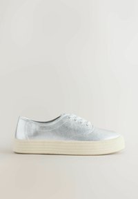 Baskets basses argentées avec lacets blancs et semelle en caoutchouc texturée épaisse de couleur beige clair, sur un fond neutre uni.