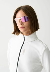 Occhiali da sole dal design elegante, con lenti a specchio viola e montatura bianca. Indossati con una giacca bianca a colletto alto con zip nera.