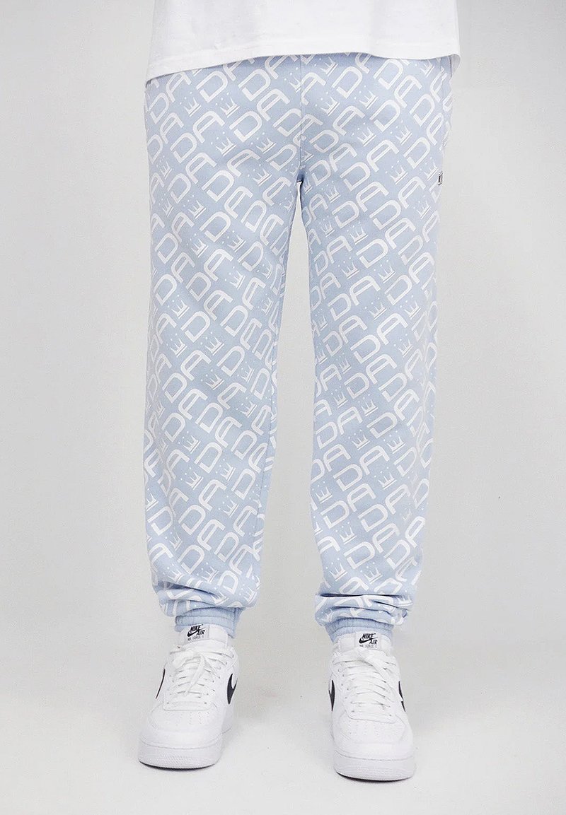 Light blue joggers with a repeating white logo pattern, featuring ribbed cuffs and a relaxed fit. Paired with white sneakers.
