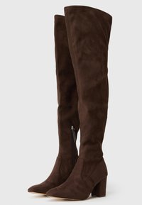 Par de botas altas de ante marrón oscuro con puntas afiladas, tacones de bloque y cremalleras laterales sobre un fondo claro y liso.