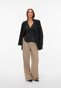 Svart satengbluse med knapper, kombinert med beige vide bukser og en svart oversized blazer, med elegante, spisse svarte hæler.