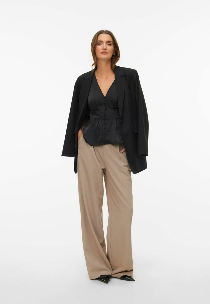 Svart satengbluse med knapper, kombinert med beige vide bukser og en svart oversized blazer, med elegante, spisse svarte hæler.