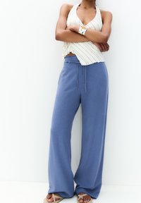 Niebieskie, szerokie spodnie wykonane z lekkiego materiału, z elastycznym paskiem w talii i detalem w postaci sznurków; zestawione z paskowanym, bezrękawnikowym topem.