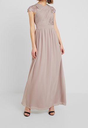 Vestido largo en taupe claro con cuerpo plisado y mangas cortas de encaje. Tela fluida con cintura ajustada y falda circular. Sandalias negras de tacón.