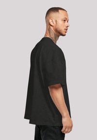 Svart oversized t-skjorte med korte ermer, laget av bomull, med rund halsutskjæring og løs passform, båret av en modell fra siden.