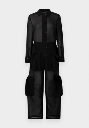 Crna prozirna kombinezona s kariranim izrezom, prednjim dugmadi, elastičnom strukom i velikim kenguruf žepovima sa strane.