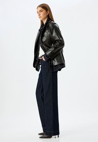 Blazer in pelle nera, maniche lunghe, chiusura con bottoni. Jeans a gamba larga blu scuro, vita alta, dettaglio sulle cuciture laterali. Tacchi a stiletto neri.