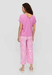 Roze top met korte mouwen, een V-rug en crisscross-detail, gecombineerd met roze gestreepte wijdlopende broek met witte bloemmotieven.