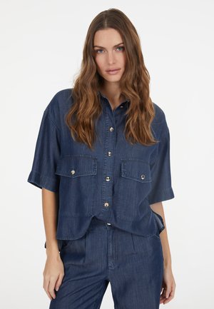 Jeanshemd in Dunkelblau, kurzärmlig, durchgehende Knopfleiste, zwei Brusttaschen und sichtbare Nähte. Glatte Textur und lässiges Design.