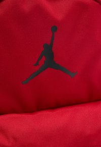 Μαύρη σιλουέτα παίκτη μπάσκετ που πηδάει με εκτεταμένο χέρι που κρατά τη μπάλα σε υφασμάτινο κόκκινο φόντο με υφή.