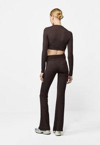 Brązowy, długi rękaw, crop top sparowany z rozszerzanymi spodniami, o dopasowanym kroju i miękkiej fakturze, noszony z jasnymi butami sportowymi.