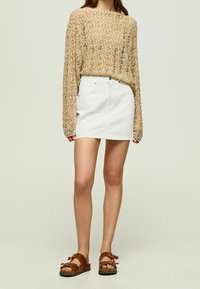 Knit beige sweater with long sleeves, paired with a white denim mini skirt. Brown sandals with buckles complete the outfit.