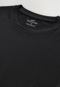 Sort bomulds t-shirt med rund hals, med et mærke der står "NEXT SIGNATURE M" og "MADE IN BANGLADESH." Blødt materiale, uden mønstre.