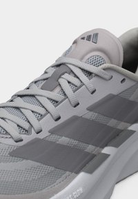 Κοντινό πλάνο ενός γκρι αθλητικού παπουτσιού με επάνω μέρος από δίχτυ, συνθετικές επικαλύψεις, κλείσιμο με κορδόνια και επενδεδυμένη σόλα με την επιγραφή "Bounce Glow".