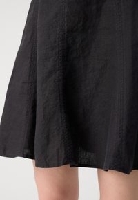 Jupe en lin noir avec un design évasé et des détails de couture visibles. L'ourlet est légèrement inégal, mettant en valeur un tissu texturé.