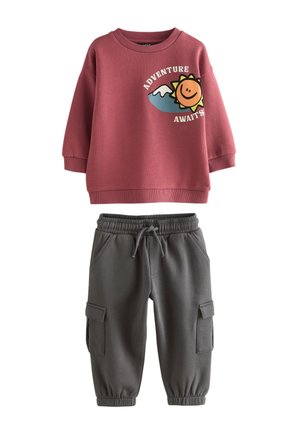 Conjunto infantil que incluye una sudadera rosa con un gráfico de sol y el texto "LA AVENTURA ESPERA", combinado con pantalones jogger grises con bolsillos cargo.