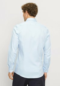 Hellblaues Langarmhemd mit Knopfkragen, glatter Textur und figurbetontem Schnitt. Verfügt über einzelne Knopfmanschetten und einen abgerundeten Saum.