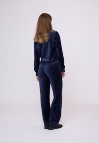 Navyblauwe fluwelen trainingspak met lange mouwen en elastische tailleband, voorzien van ribgebreide manchetten en een ontspannen pasvorm. Glad textuur, minimale details.