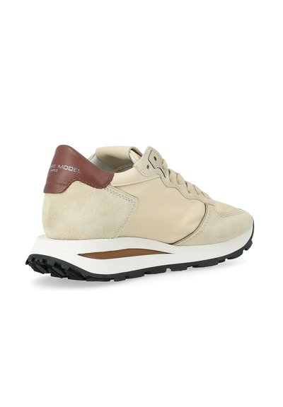 Sneaker beige e marrone con dettagli in suede e pelle, suola bianca, battistrada nero e lacci, angolata per mostrare il lato esterno e il marchio sul tallone.