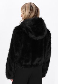 Schwarze Fake-Fur-Hoodie-Jacke mit Kapuze, cropped Design und langen Ärmeln. Die Textur wirkt weich und flauschig. Keine sichtbaren Hardwaredetails.