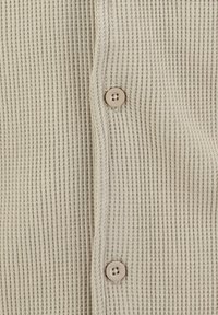 Close-up van beige wafelbreisel met een verticale naad en twee kleine beige knopen genaaid.