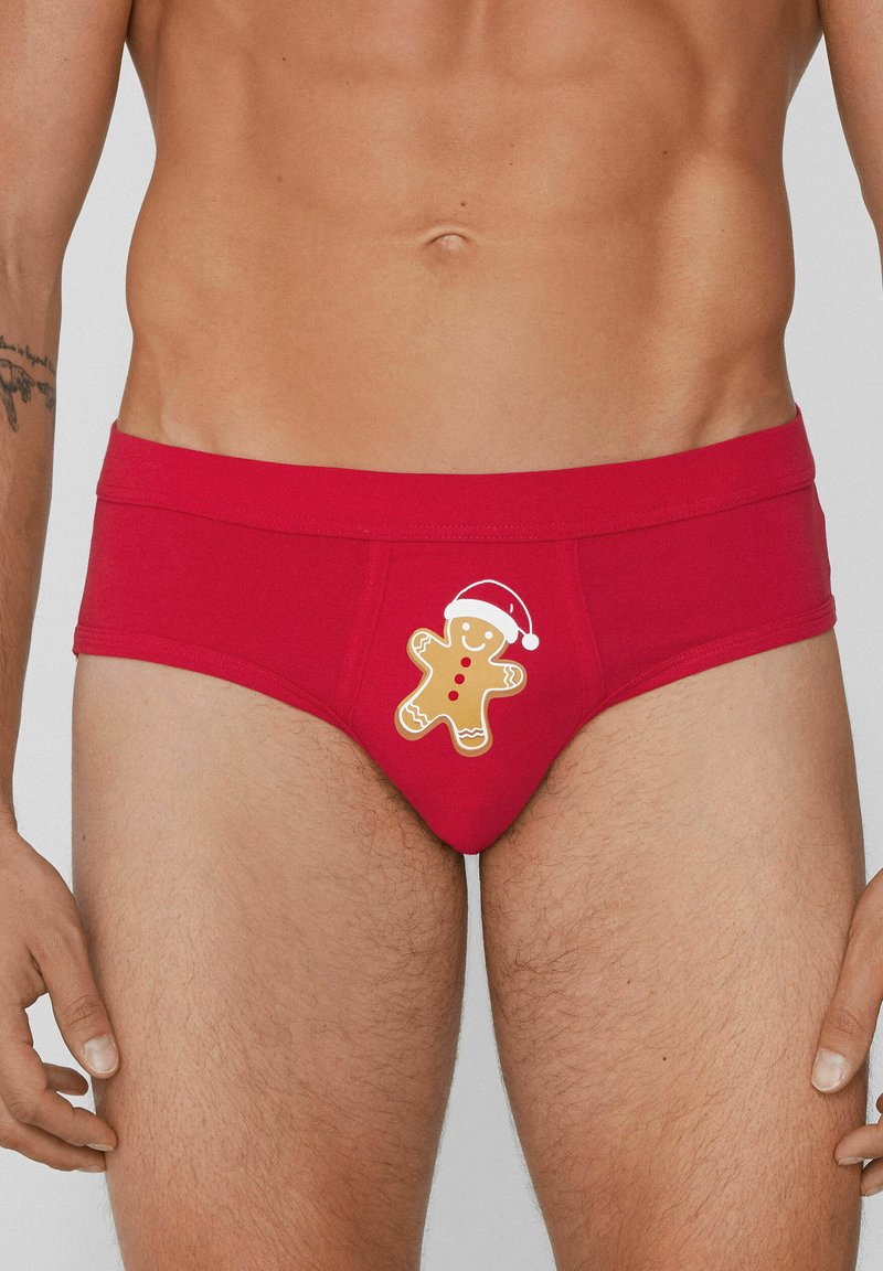 Rote Baumwoll-Slips mit einer Grafik eines Lebkuchenmanns mit Weihnachtsmannmütze auf der Vorderseite. Glatte Textur mit elastischem Bund.