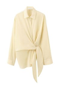 Žuta majica v stilu ovijanja z ovratnikom, dolgimi rokavi in subtilnimi vertikalnimi črtami, pritrjena s pašnim trakom v pasu.