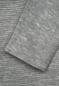 Tissu tricoté gris avec un motif texturé, présentant des nuances de gris variées. Fini lisse avec un bord replié montrant des détails de couture.
