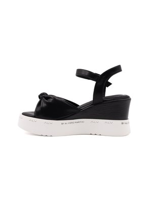 Sandales compensées noires avec un design à l'avant noué, dessus en synthétique, bride réglable autour de la cheville et une semelle plate-forme texturée blanche.