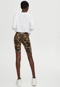 Fietsbroek in camouflagemotief in tinten bruin en groen, nauwsluitend ontwerp, tot halverwege de dij, gecombineerd met een effen witte top met lange mouwen.