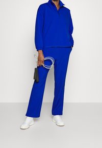 Blauw sportief set, bestaande uit een pullover met rits en bijpassende broek, met een comfortabele pasvorm en afgewerkt met witte sneakers en een springtouw.