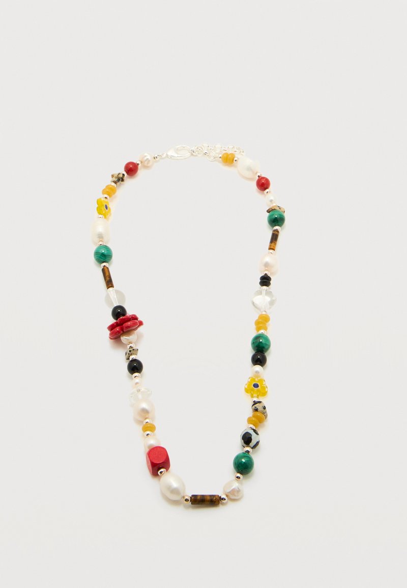 Collier avec des perles variées en rouge, vert, jaune, noir et blanc, incluant des perles, des fleurs et des formes géométriques sur une chaîne en argent.