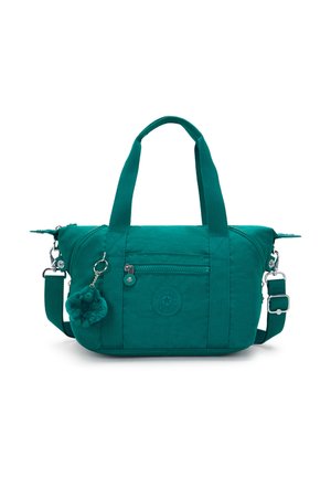 Teal fabric bag with dual handles and a removable shoulder strap, features zippered pocket, logo patch, and a pom-pom charm.