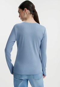Dugi rukav, rebrasti top svijetloplave boje, s okruglim izrezom i slim fit krojem. Uparen s svijetloplavim trapericama za kontrast.