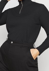 Sorte ribbede turtleneck med halv-zip-design, der har langeærmer og en tætsiddende silhuet, parret med højtsiddende sorte bukser.