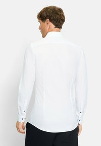 Weißes Langarmhemd mit schmalem Schnitt, klassischem Kragen und geknöpften Manschetten mit blauen Akzenten. Glattes, leichtes Material.
