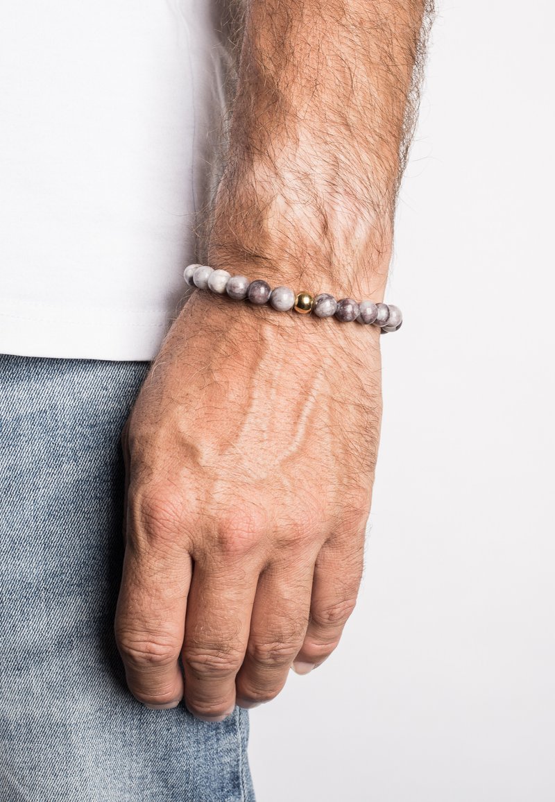 Grey and white stone bead bracelet with a single gold accent bead, worn on a wrist with light skin and visible hair.