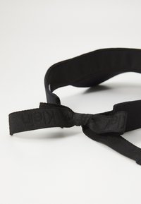 Zwart stoffen haarband met een vlak ontwerp, voorzien van een geknoopte accent en verhoogde branding. Zachte textuur met een subtiele glans.