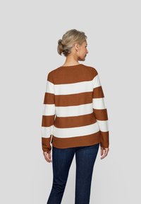 Braun-weiß gestreifter Langarmpullover mit Rundhalsausschnitt und seitlichen Schlitzen, getragen über dunkelblauen Jeans. Die Rückansicht zeigt die Textur und das Design.