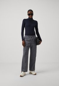 Marinefarbener Rollkragenpullover, graue, maßgeschneiderte Cargo-Hosen und weiße Sneakers. Als Accessoires dienen schwarze Sonnenbrillen und eine schwarze Handtasche.