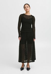 Completo in pizzo nero composto da top e gonna con maniche lunghe, motivo testurizzato e lunghezza alla caviglia. Presenta una vita aderente e un design a strati.